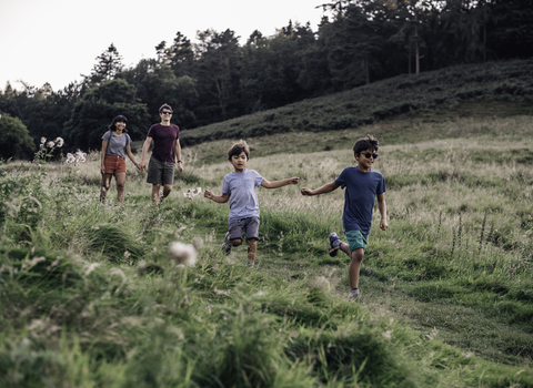 2 adults and 2 children walk down a grassy hill surrounded by trees